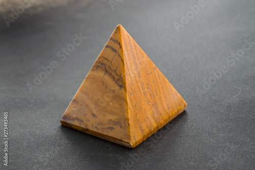 Tiger eye stone in the shape of a pyramid close-up on a black background for jewelry