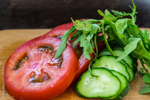 Sliced ​​tomatoes and parsley with cucumbers for salad, vegetarian food on a cutting board