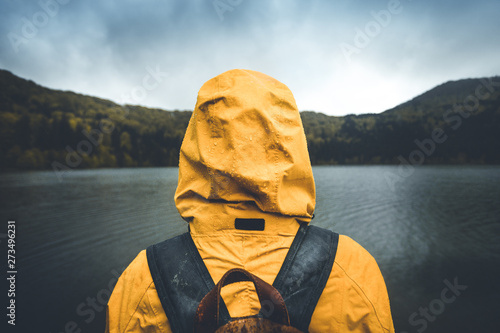 Active outdoors people lifestyle. Rear view of a hiker enjoying rainy weather. Outdoors adventure trek activity, hiker wearing yellow waterproof raincoat sportswear clothes