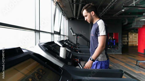 Young man in sportswear running on treadmill at gym. Healthy lifestyle and sports concept