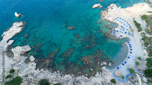 Sunny beach lagoon with rocky coastline, Greece. Tourists under umbrella chill relax near clear blue emerald turquoise sea water