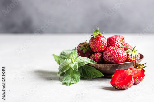 Strawberries in a wooden bowl with mint on a light grey stone table.