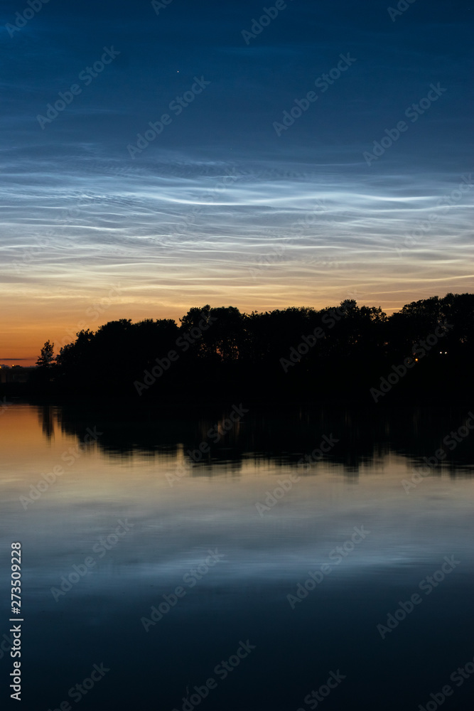 Noctilucent clouds (night shining clouds): blue silvery colored clouds in the upper atmosphere over a dutch lake close to Gouda, Holland.