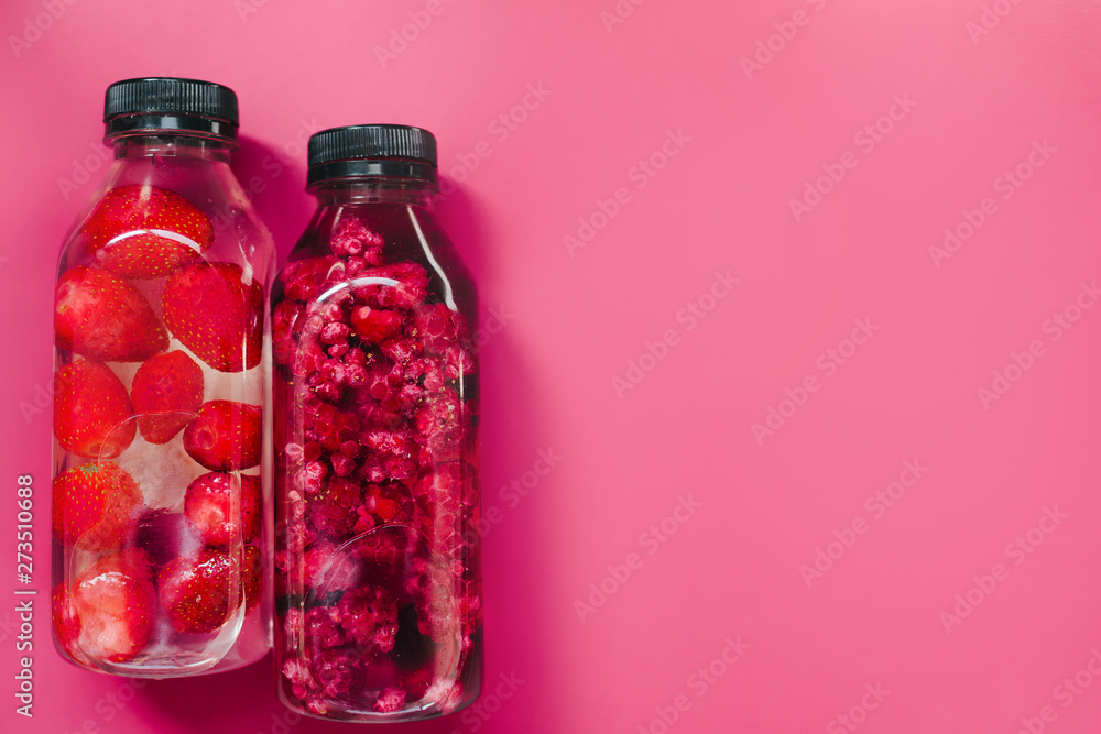 Detox infused fresh water with strawberry raspberries in sparkling glasses and bottle on colorful pink background, copy space. Cold summer drink. Mineral water. Top view, flat lay Detox infused fresh water with strawberry raspberries in sparkling glasses and bottle on colorful pink background, copy space. Cold summer drink. Mineral water. Top view, flat lay