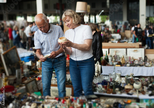 Glad man and woman choosing interesting souvenirs at traditional flea market