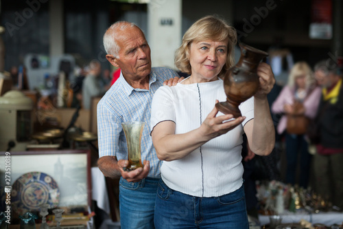 Smiling mature spouses buying retro handicrafts on flea market