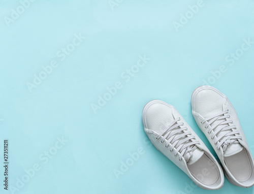 White leather sneakers on blue background. Pair of fashion trendy white sport shoes or sneakers with copy space for text or design. Overhead shot of new white sneakers. Top view or flat lay.