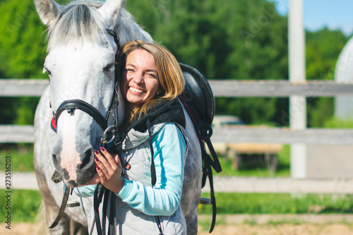 Beautiful cute sexy slim girl jockey with a beautiful smile next to a gray horse in spots in nature on a clear Sunny summer day