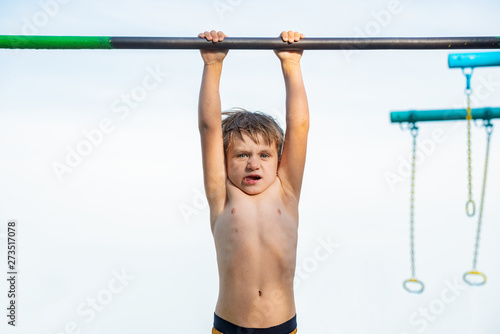 A little boy is hanging on the horizontal bar and can not do anything.