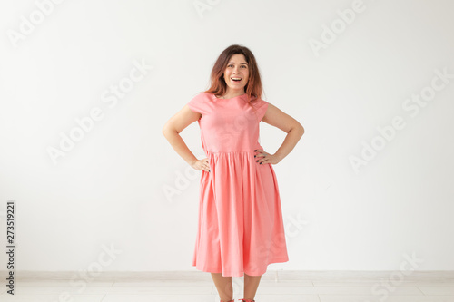 Beautiful young cheerful woman in a long peach dress posing on a white wall. Concept of stylish young woman. Copy space