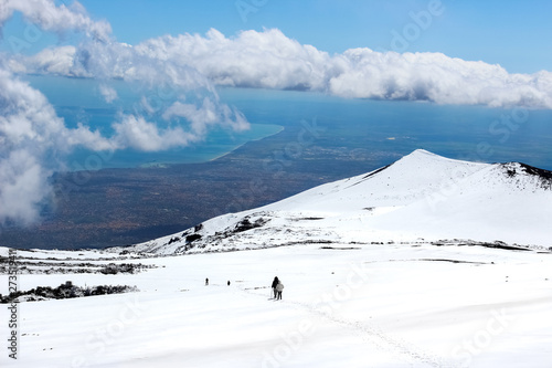 Amazing view from Mount Etna photographed with hikers going down on the snow and sea coast in the background. Magnificent clouds close to the top of the mountain. Etna, Sicily, Italy