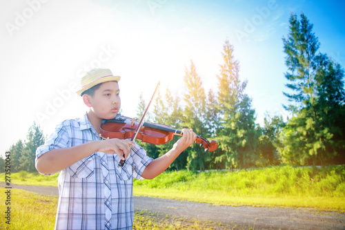 Little boy playing violin, learning and practicing in the natural garden. He is happy.