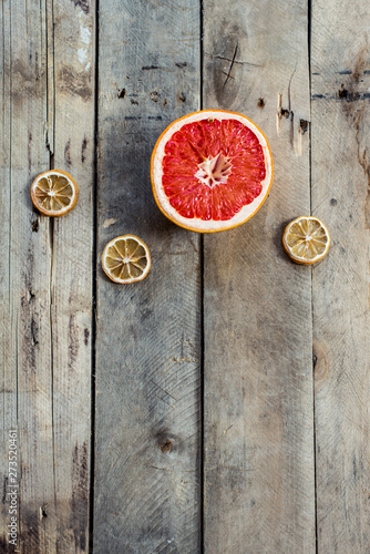 One half of red ripe grapefruit and three slices of dry decorative tangerines on an old wooden retro background in vintage style. Falling fruit. trendy flatlay. stylish food photography. Copy spase