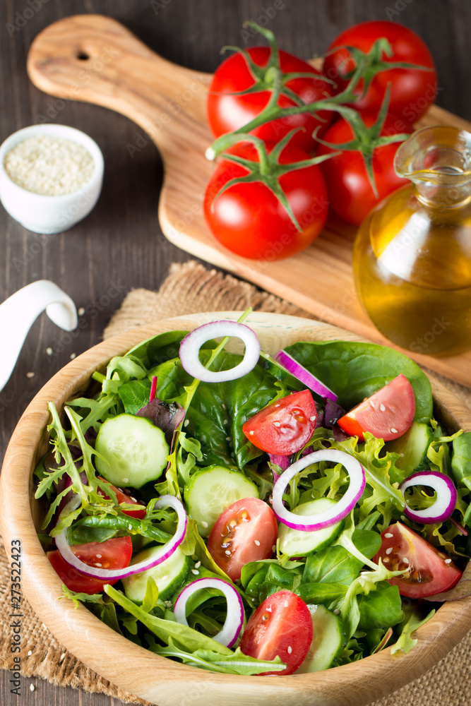 Fresh healthy vegetable salad made of cherry tomato, ruccola, arugula, feta, olives, cucumbers, onion and spices. Greek, Caesar salad in a bowl on wooden background. Healthy organic food concept.