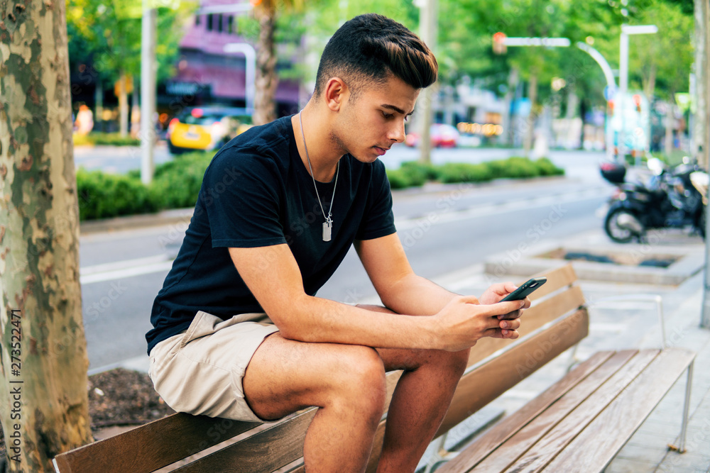 Young fashionable handsome man on the street of modern city chatting and typing on a cell phone. Communication and messenger concept