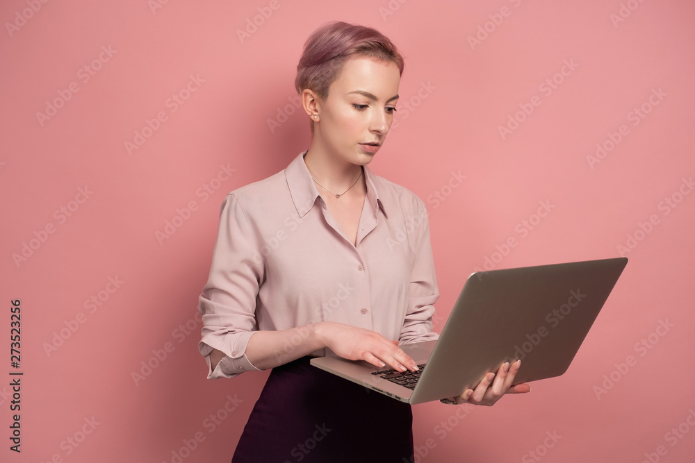 Pink-haired young woman works with her laptop, pink background Pink-haired young woman works with her laptop, pink background