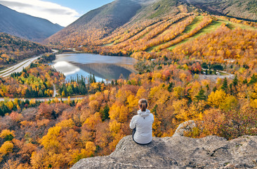 Woman hiking at Artist's Bluff in autumn. View of Echo Lake. Fall colours in Franconia Notch State Park. White Mountain National Forest, New Hampshire, USA