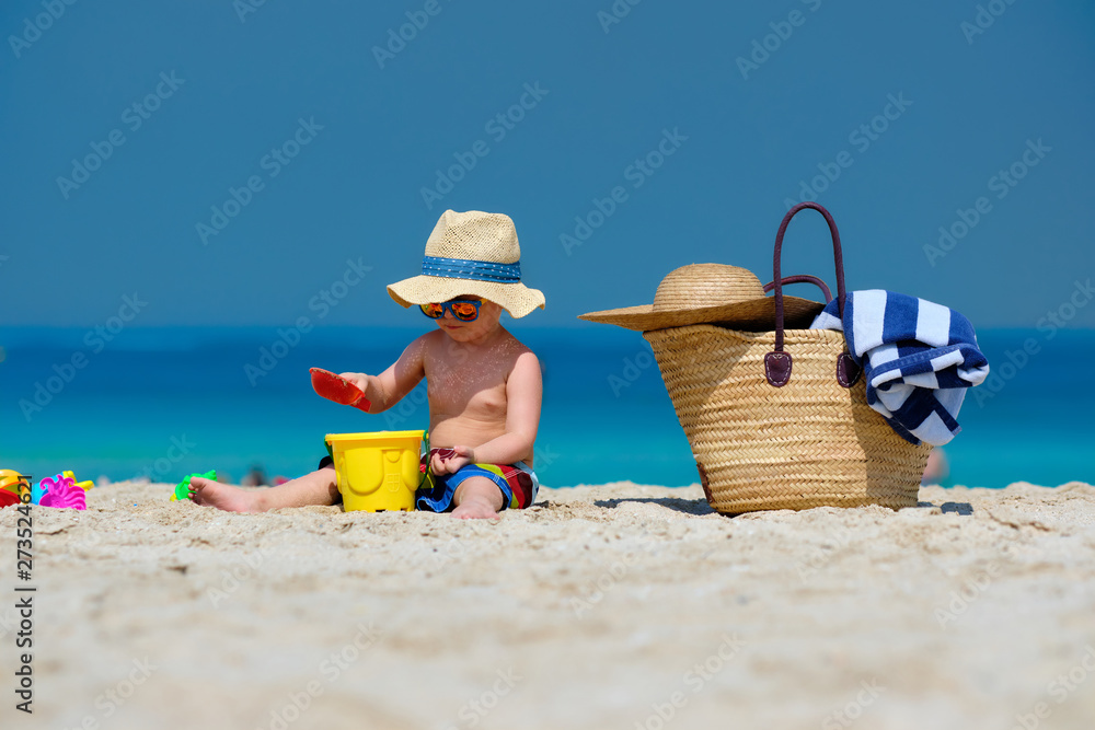 Two year old toddler boy playing with beach toys on beach