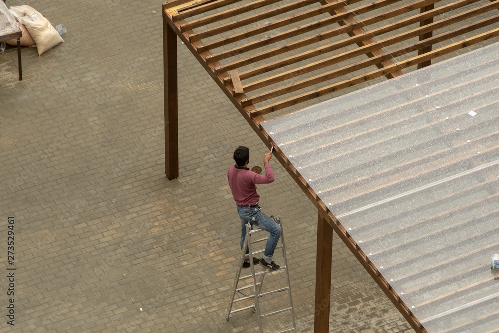 Male worker on a stepladder paints a wooden building