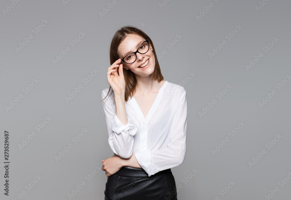 Portrait of young modern business woman. Smiling beautiful slim brunette with equal hair female business leader in casual wear expressing happy emotions. Gray background. Portrait of young modern business woman. Smiling beautiful slim brunette with equal hair female business leader in casual wear expressing happy emotions. Gray background.