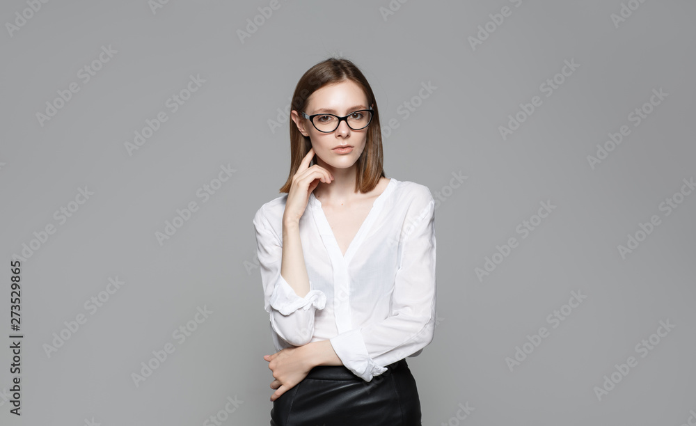 Portrait of the young modern business woman. The strict beautiful thin brunette with the equal business leader of the woman of hair in casual clothes. Gray background. Portrait of the young modern business woman. The strict beautiful thin brunette with the equal business leader of the woman of hair in casual clothes. Gray background.
