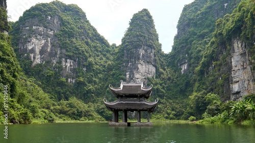 Small temple on the river surrounded by karst mountains. Beautiful landscape during the Trang An boat tour in Tam Coc, Vietnam.