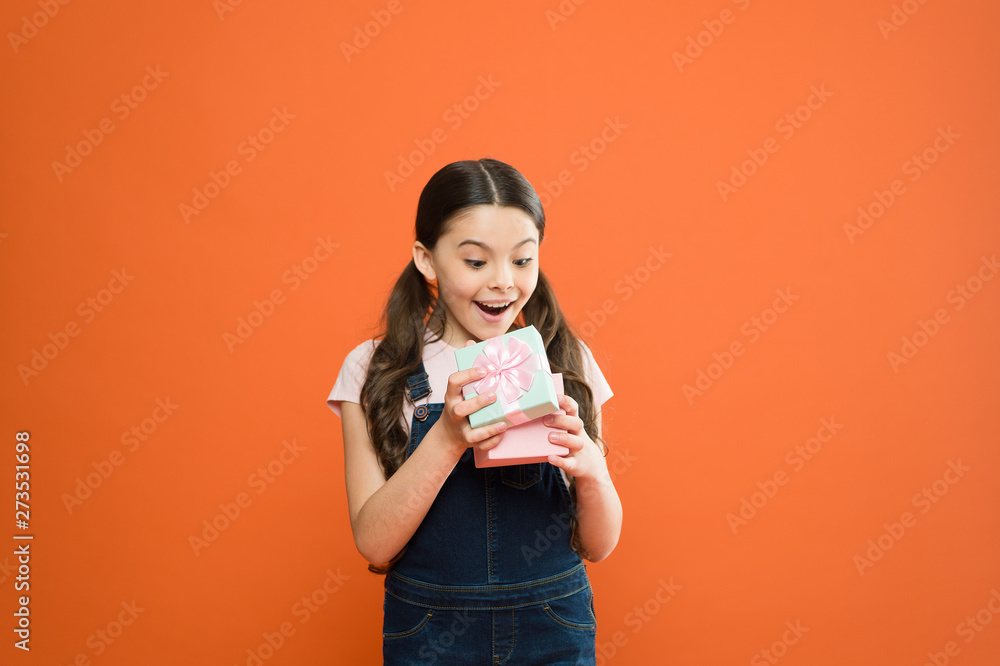 It caught her by surprise. Cute small child opening gift box with surprise face on orange background. Adorable little girl getting birthday surprise. Being shocked of pleasant surprise