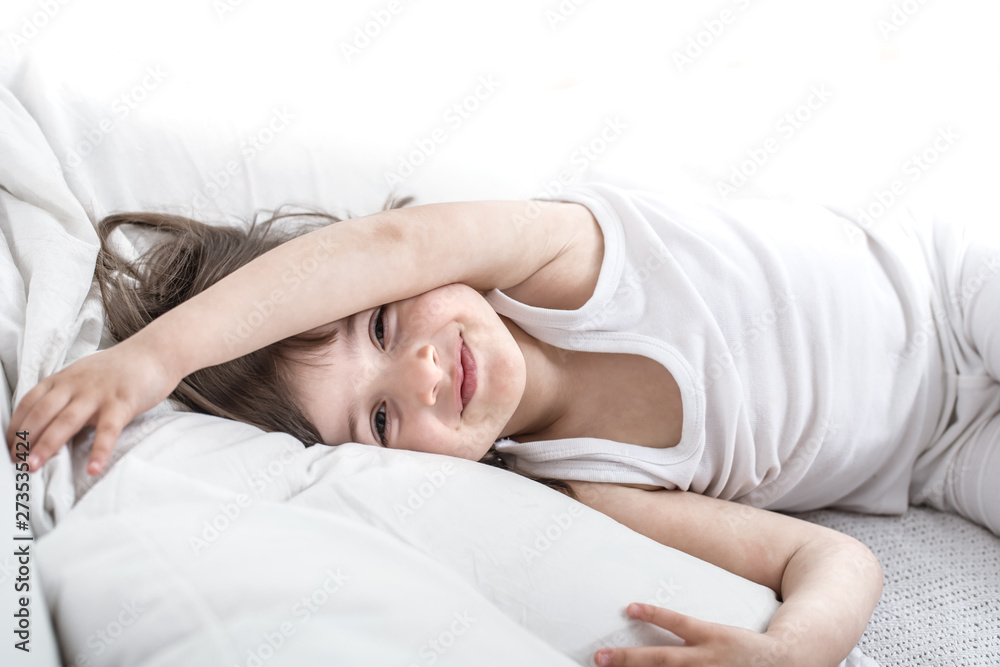 Cute little girl smiling while lying in a cozy white bed Cute little girl smiling while lying in a cozy white bed