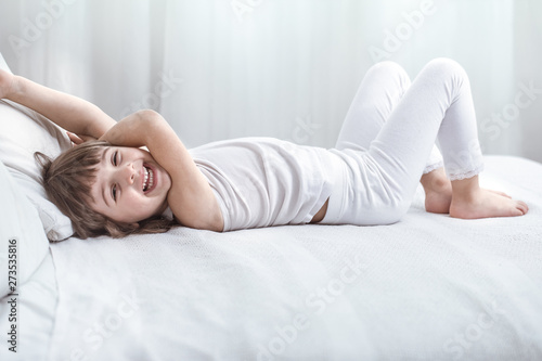 Cute little girl smiling while lying in a cozy white bed