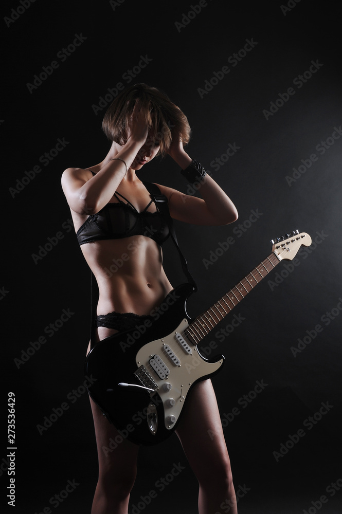 Beautiful sexy girl with electric guitar on a black background, backlight
