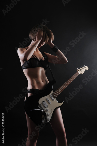 Beautiful sexy girl with electric guitar on a black background, backlight