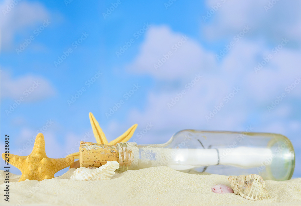 Summertime image of a beach scene on sand with a blue sky that has puffy white clouds in the distance. A message in a bottle lays among shells and starfish.