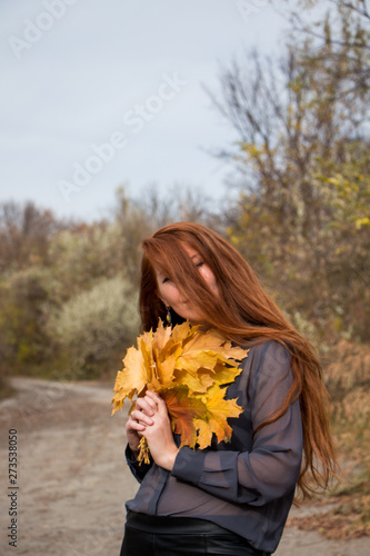 Portrait of young redhead woman with bouquet of yellow leaves