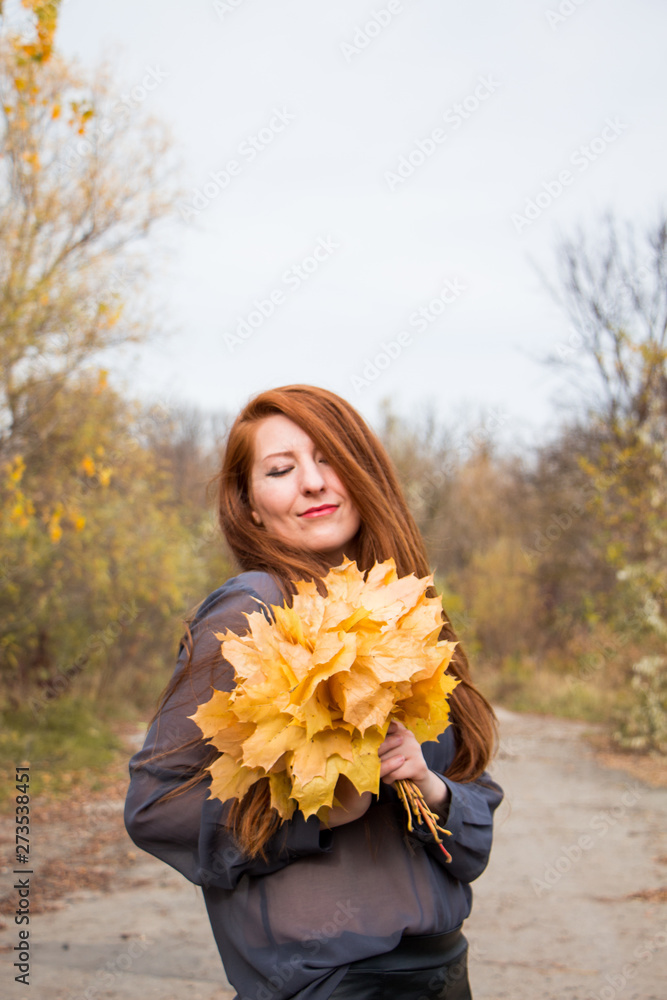 Naklejka premium Portrait of young redhead woman with bouquet of yellow leaves