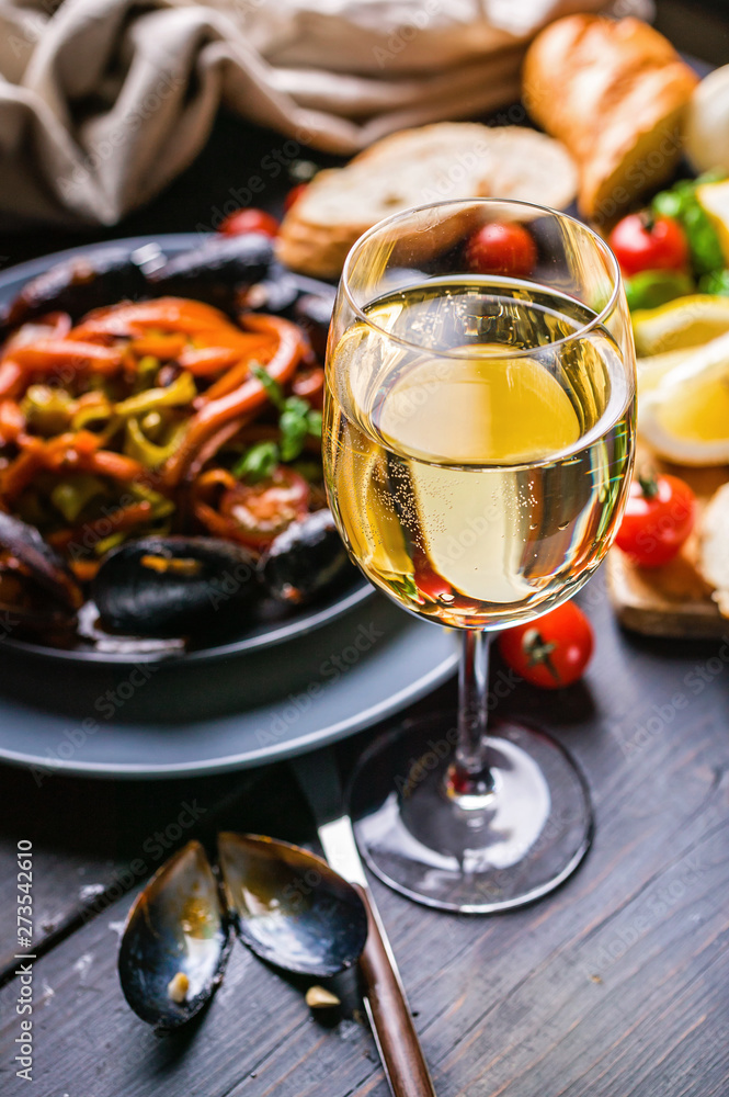 A glass of dry white wine on the background of Italian cuisine. Pasta, mussels and wine.
