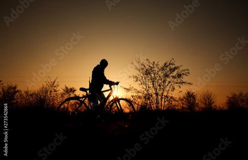 Silhouette of a boy with bicycle on background of bright sunset sun in vintage old style