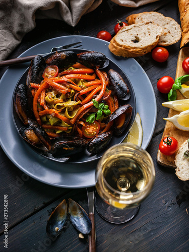 Top view Italian pasta. Mussels and vegetables. White wine. Close-up. Traditional Mediterranean cuisine. Dark wooden background