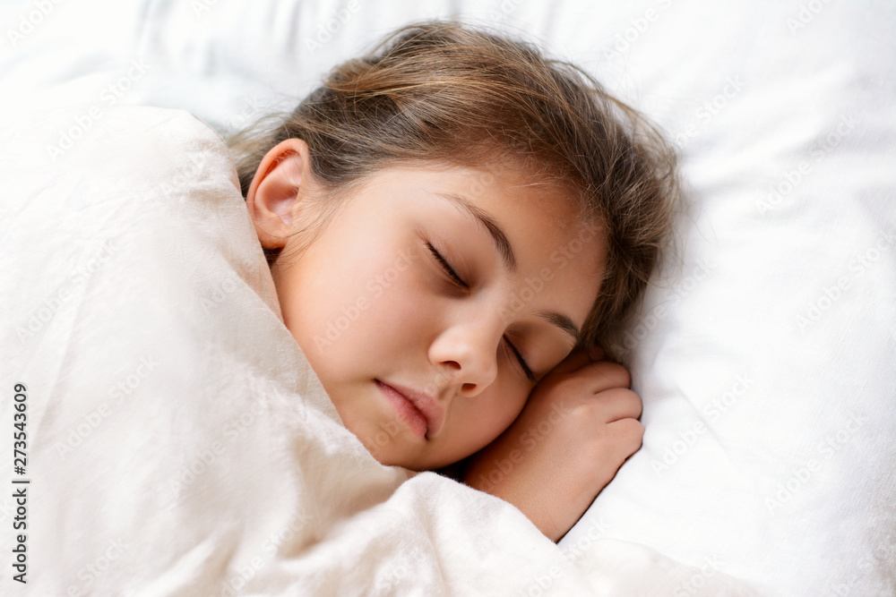 Lovely little girl sleeping on comfortable bed covered with soft warm blanket at night. Young female child with natural dark hair lies on bed Lovely little girl sleeping on comfortable bed covered with soft warm blanket at night. Young female child with natural dark hair lies on bed