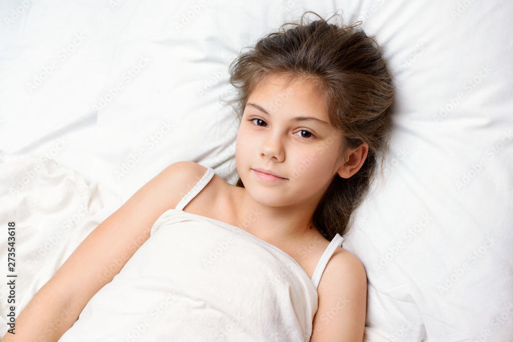 Lovely little girl has awoken early in the morning full of power with a burning desire to go to school and studying. Beautiful small female girl lies on comfortable bed Lovely little girl has awoken early in the morning full of power with a burning desire to go to school and studying. Beautiful small female girl lies on comfortable bed