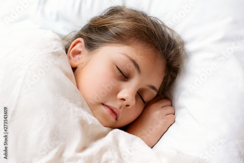 Lovely little girl sleeping on comfortable bed covered with soft warm blanket at night. Young female child with natural dark hair lies on bed