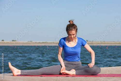 Girl practicing yoga near lake, enjoying nice day in nature and positive energy.