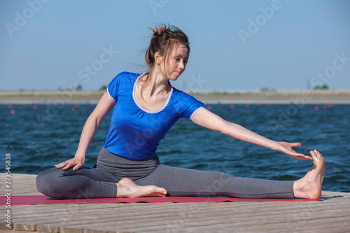 Girl practicing yoga near lake, enjoying nice day in nature and positive energy.