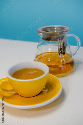 Yellow cup of tea and glass teapot on the table. Blue background