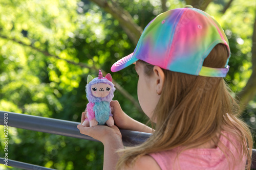 Colored plush llama unicorn in hands little girl with greens on background photo