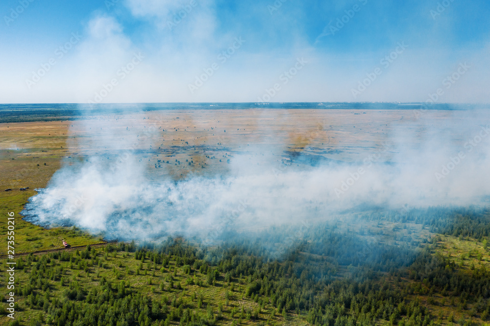 Aerial view of wildfire in green fields from hot weather, natural disaster accident, burning forest and huge clouds of smoke