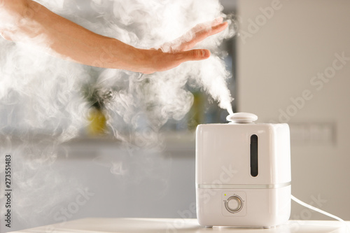 man holds hand over steam aroma oil diffuser on the table at home, steam from the air humidifier, free space. Ultrasonic technology, increase in air humidity indoors, comfortable living conditions photo