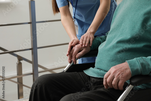 Nurse assisting senior man in wheelchair at hospital, closeup