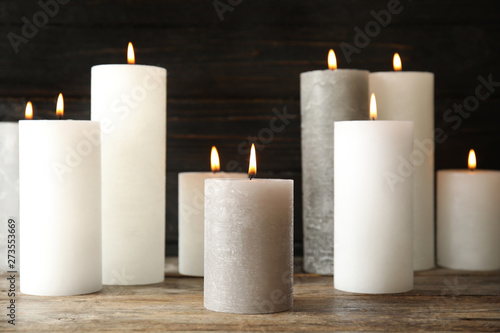 Many alight wax candles on table against dark background