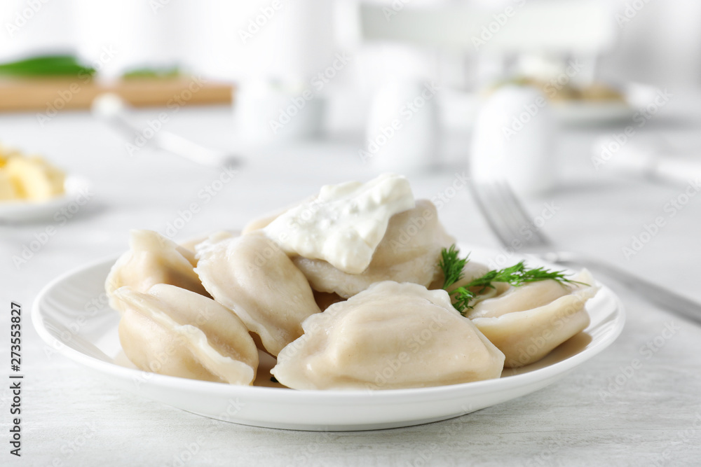 Plate of tasty dumplings served with sour cream and dill on table Plate of tasty dumplings served with sour cream and dill on table