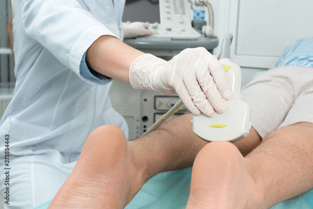 Doctor conducting ultrasound examination of patient's foot in clinic, closeup